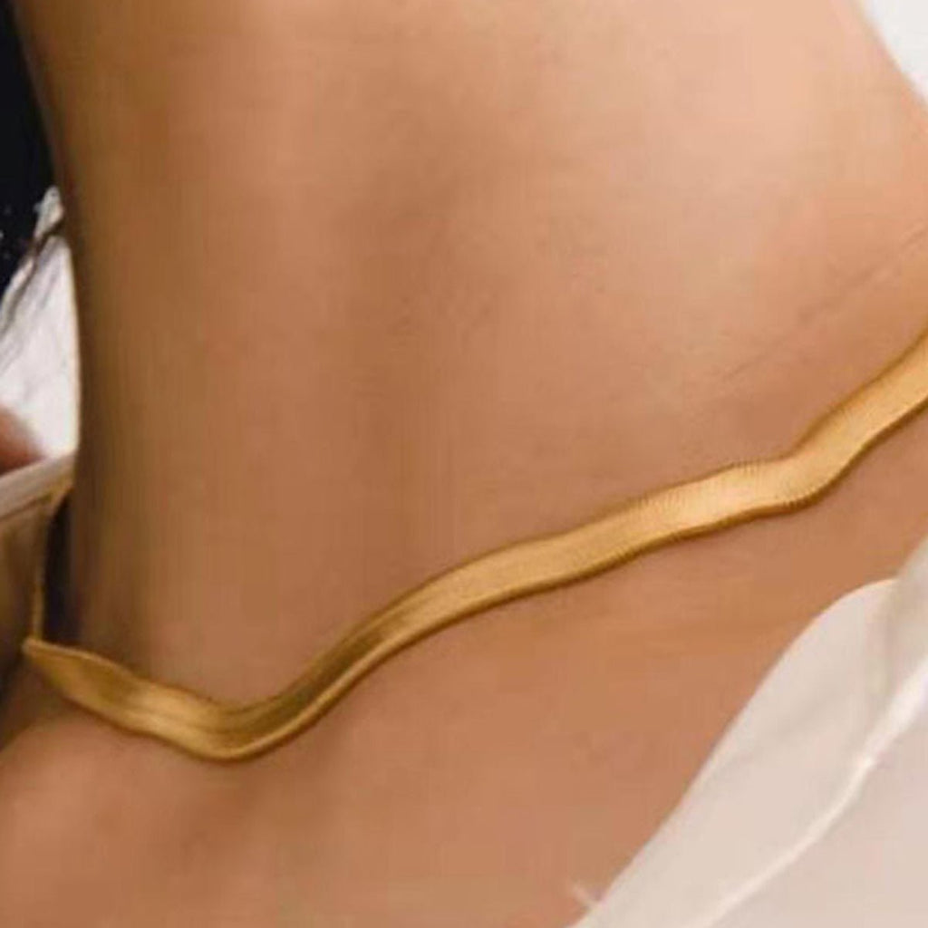 Gold anklet on a person's ankle against a neutral background