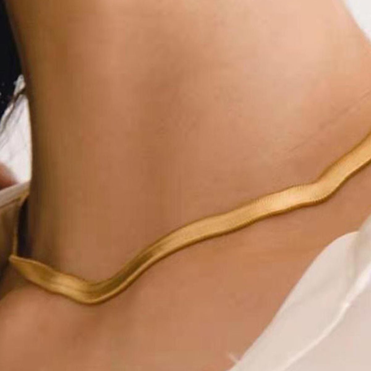 Gold anklet on a person's ankle against a neutral background