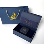 Open navy blue gift box with a black square item inside, accompanied by a matching navy blue bag with gold logo.