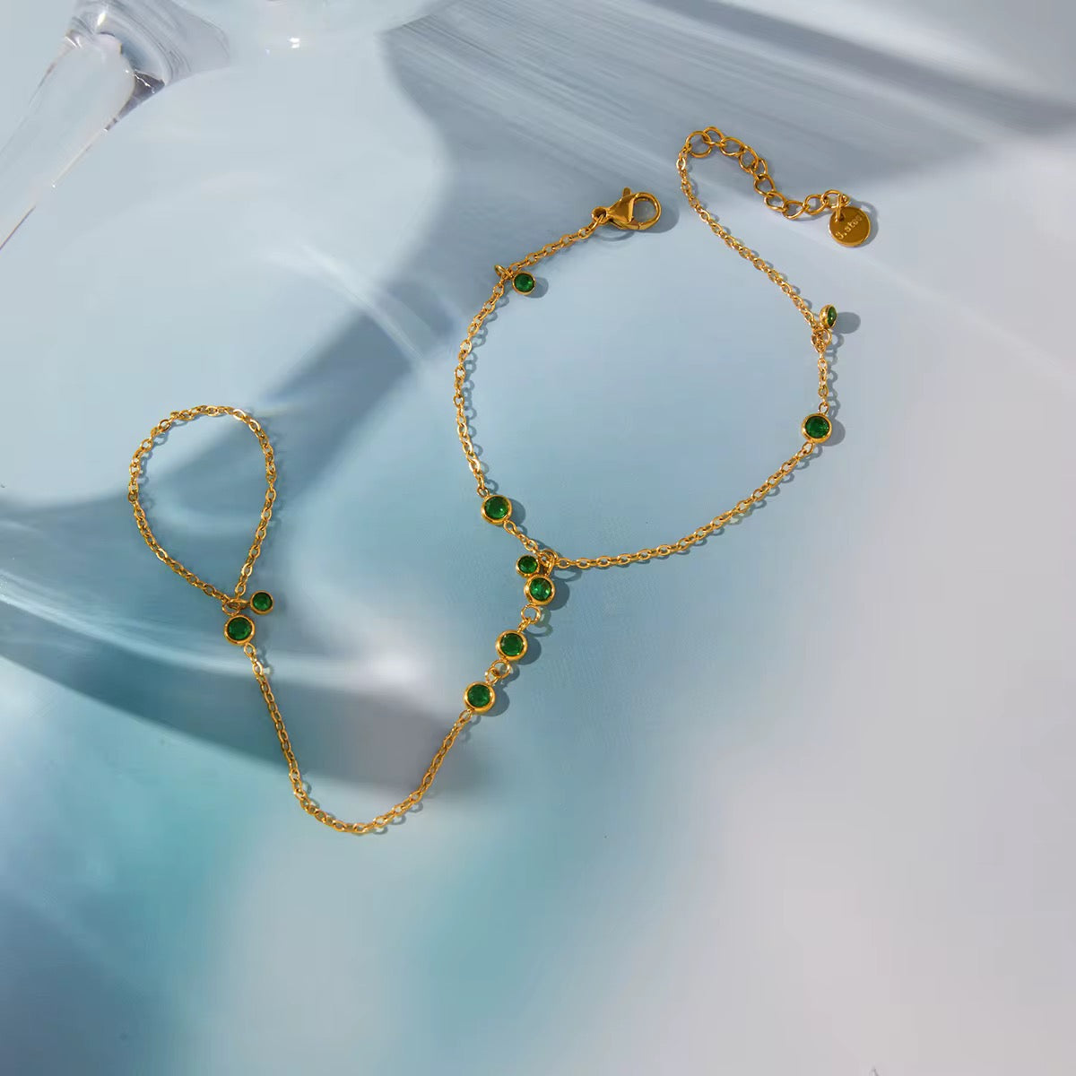 Emerald Trace hand chain featuring 18k gold PVD plated stainless steel and green crystals.