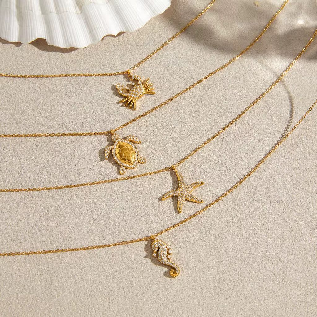 Gold necklaces with sea-themed pendants on a beige surface