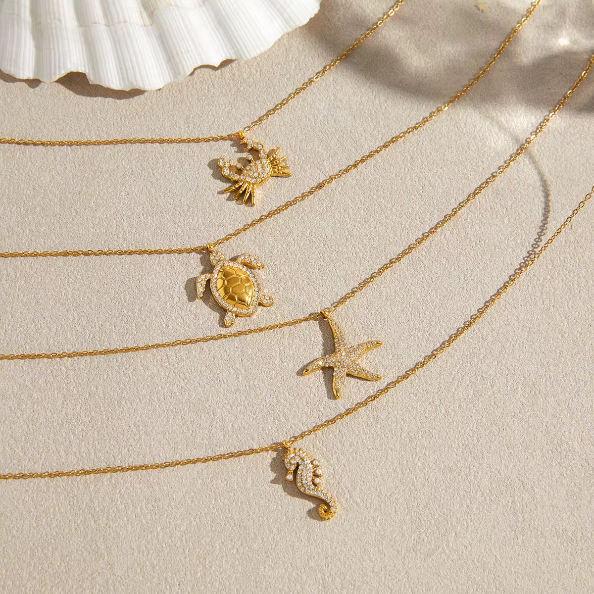 Gold necklaces with sea-themed pendants on a beige surface