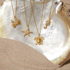 Gold necklaces with sea-themed pendants on a shell and sand background
