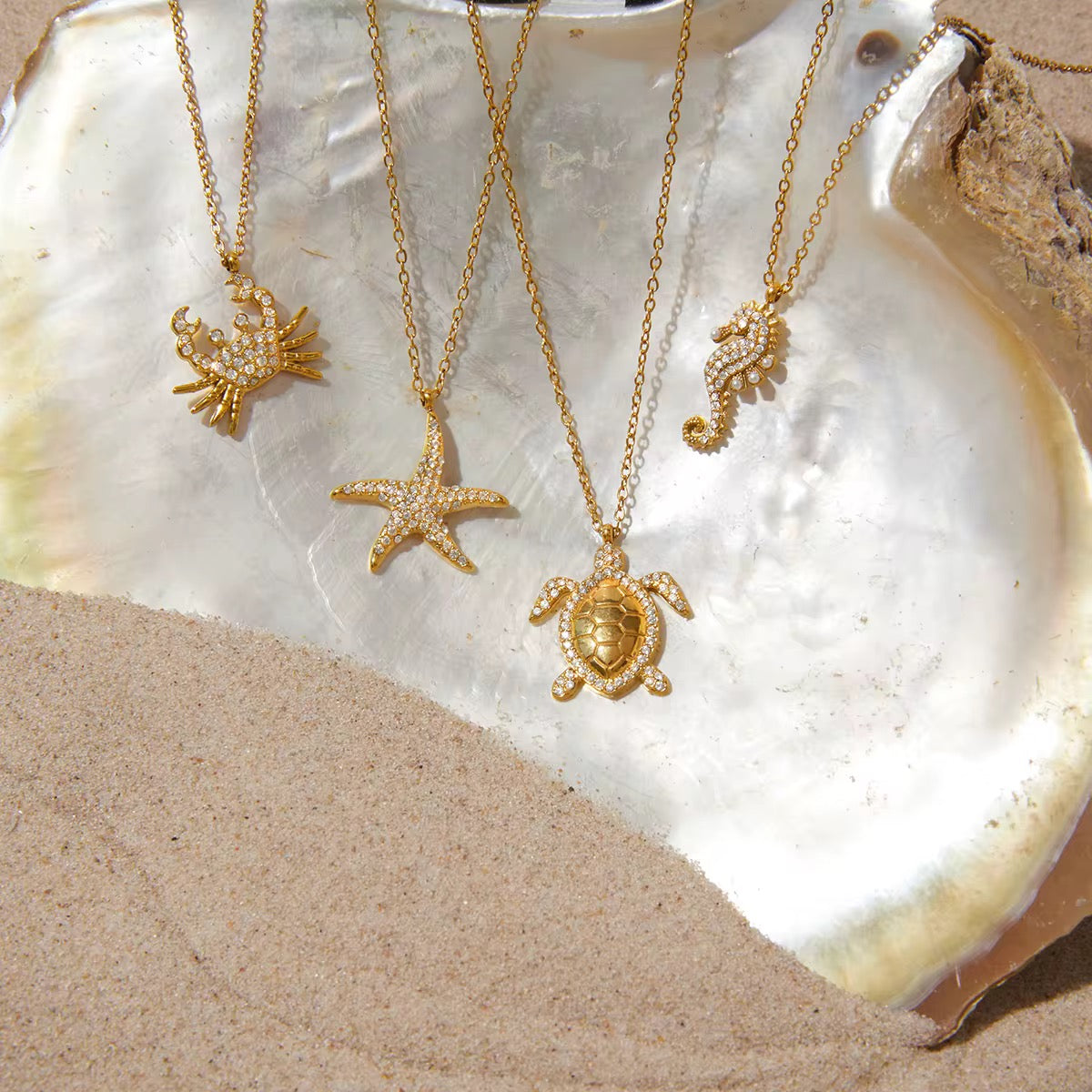 Gold necklaces with sea-themed pendants on a shell and sand background