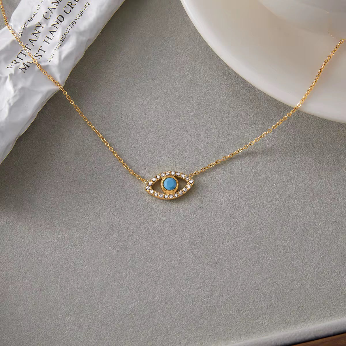 Detail of the delicate crystal-encrusted evil eye pendant on a gold link chain.