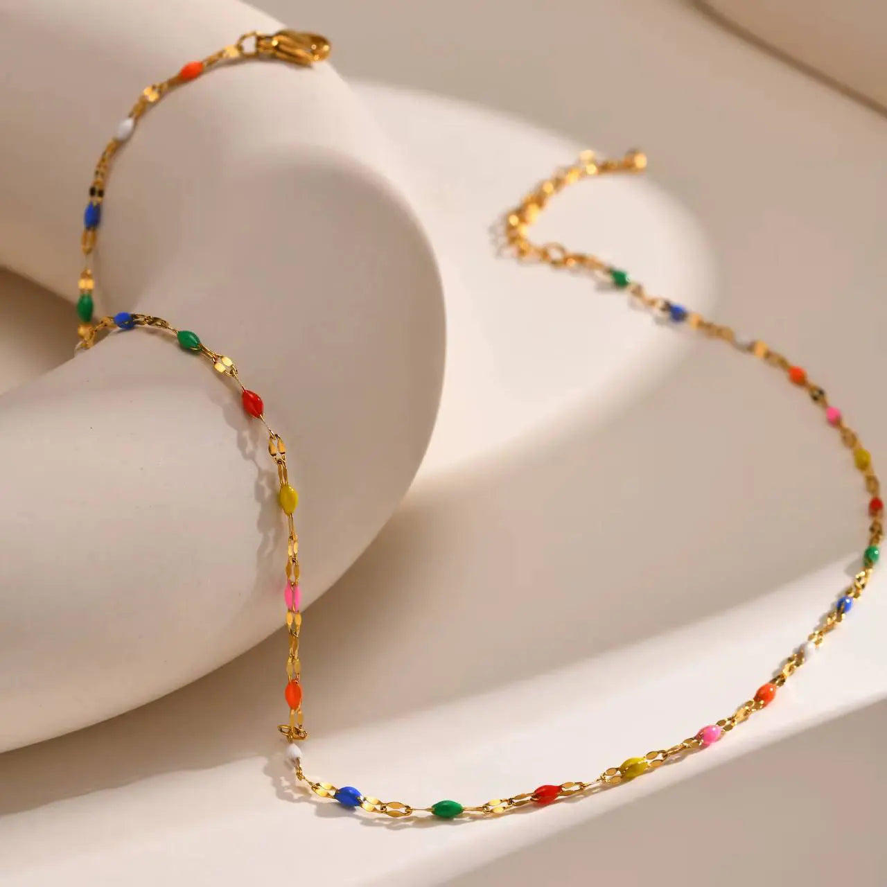 Malibu multi-color enamel lip chain choker necklace in 18k gold PVD plated stainless steel on a white sculpted display.