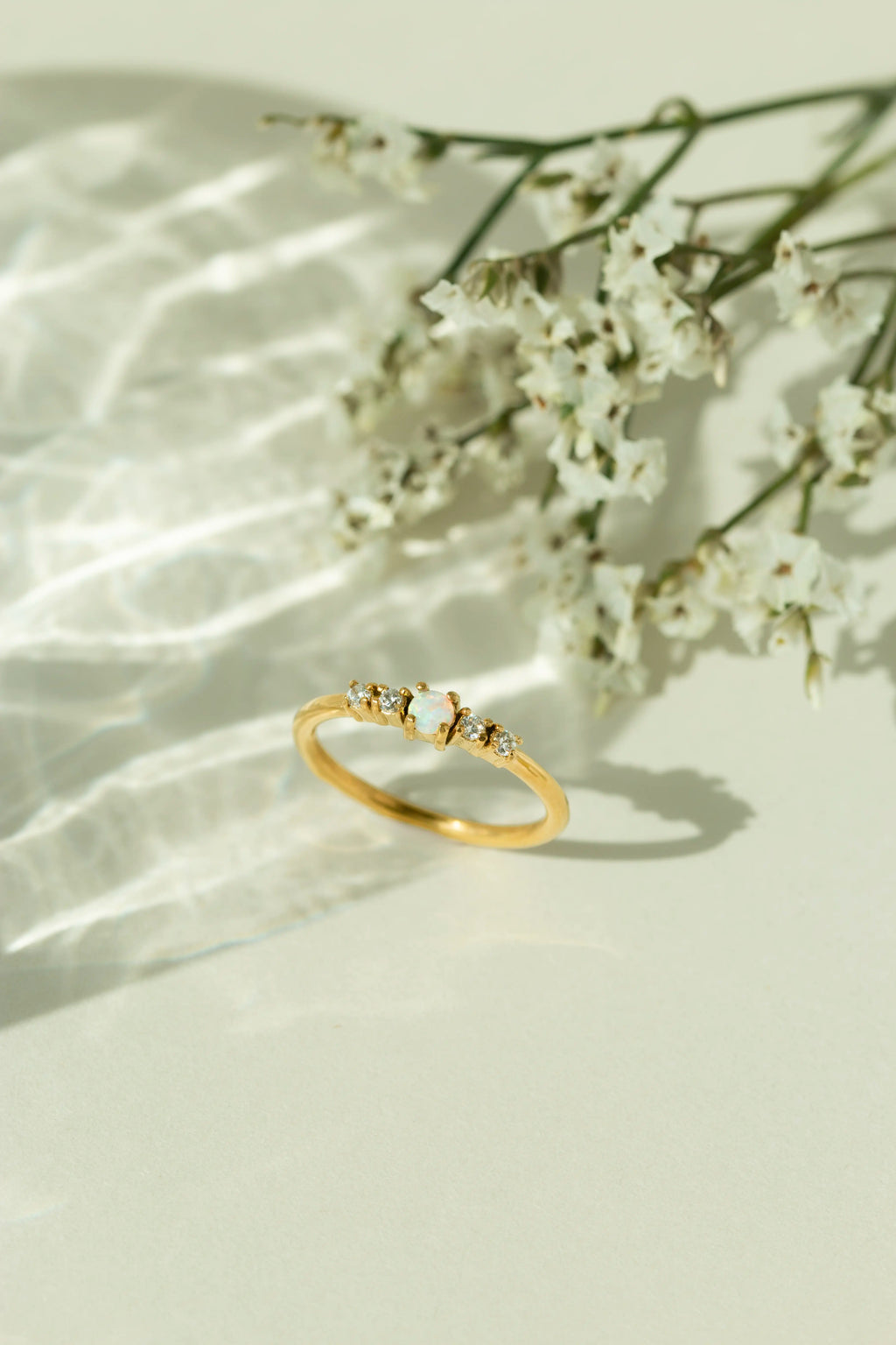 Minimalist 14k gold natural opal ring with diamond accents displayed next to white flowers under soft sunlight. Perfect dainty gemstone promise ring or stackable gold jewelry for women.