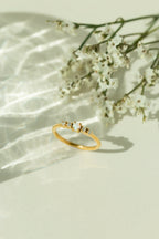 Minimalist 14k gold natural opal ring with diamond accents displayed next to white flowers under soft sunlight. Perfect dainty gemstone promise ring or stackable gold jewelry for women.