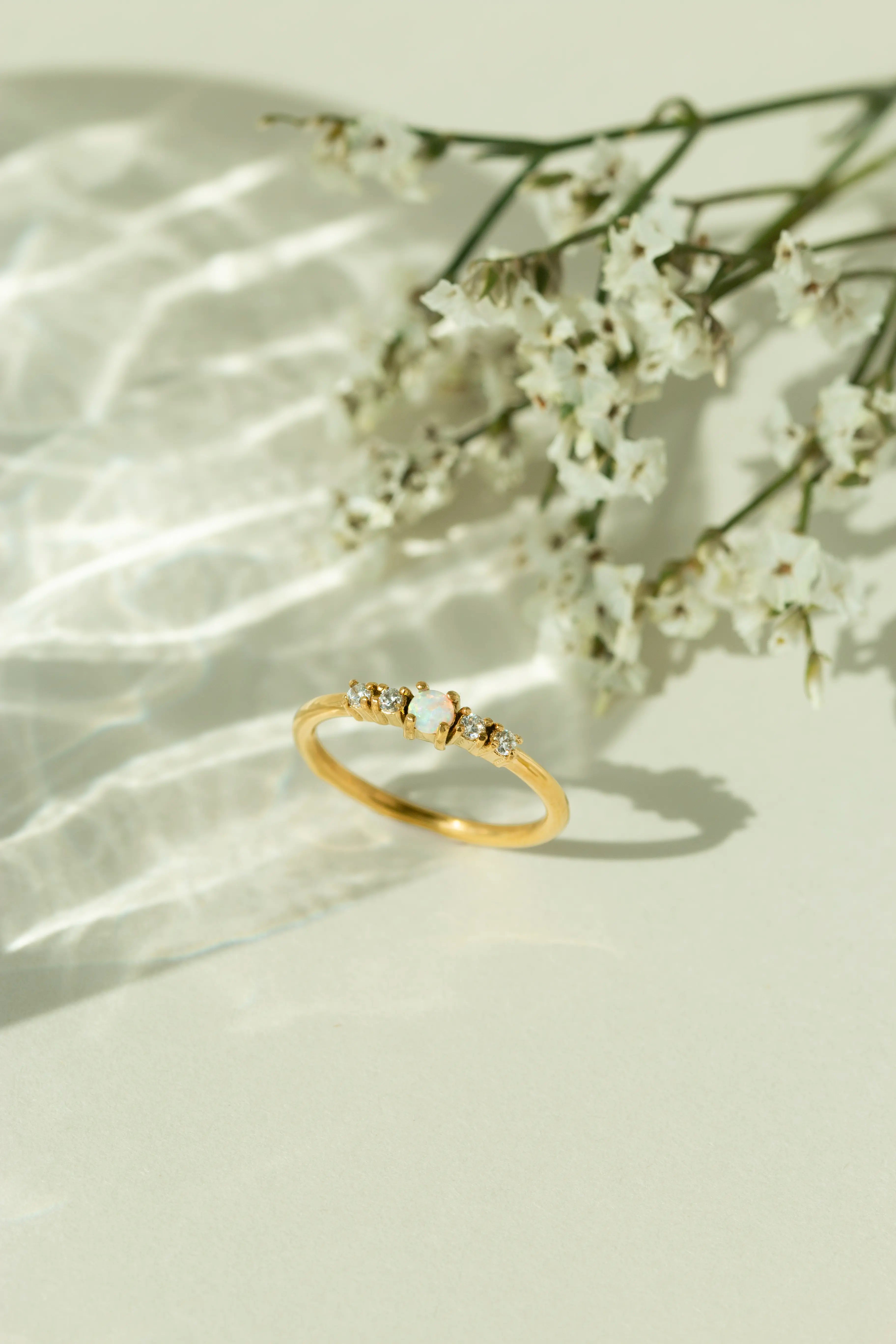 Minimalist 14k gold natural opal ring with diamond accents displayed next to white flowers under soft sunlight. Perfect dainty gemstone promise ring or stackable gold jewelry for women.