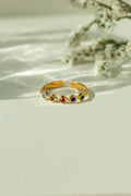 Gold adjustable multi color gemstone ring with colorful birthstones in diamond shaped settings. Trendy open back stackable band displayed on a sunlit neutral background.