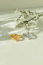 Gold and silver starburst signet rings featuring a central diamond accent stone. Chunky minimalist celestial jewelry styled on a light surface with white flowers.