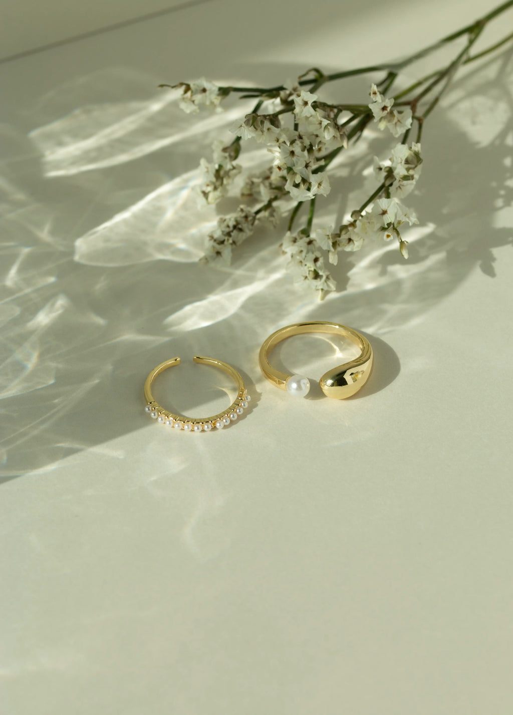 Minimalist 14k gold open pearl ring and chunky gold dome ring with a fresh water pearl accent. Elegant dainty seed pearl ring set styled next to white flowers under soft sunlight.