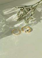 Minimalist 14k gold open pearl ring and chunky gold dome ring with a fresh water pearl accent. Elegant dainty seed pearl ring set styled next to white flowers under soft sunlight.
