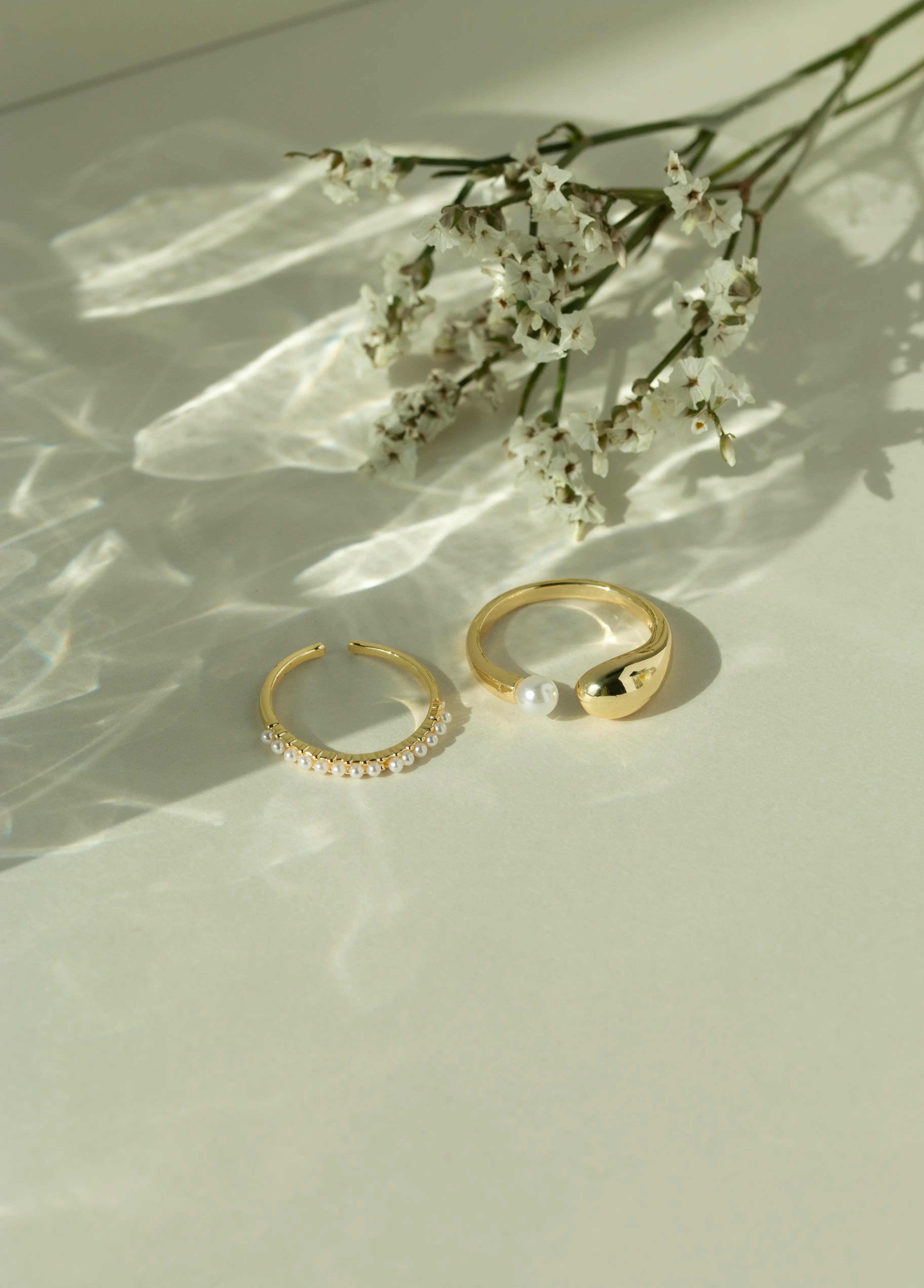 Minimalist 14k gold open pearl ring and chunky gold dome ring with a fresh water pearl accent. Elegant dainty seed pearl ring set styled next to white flowers under soft sunlight.