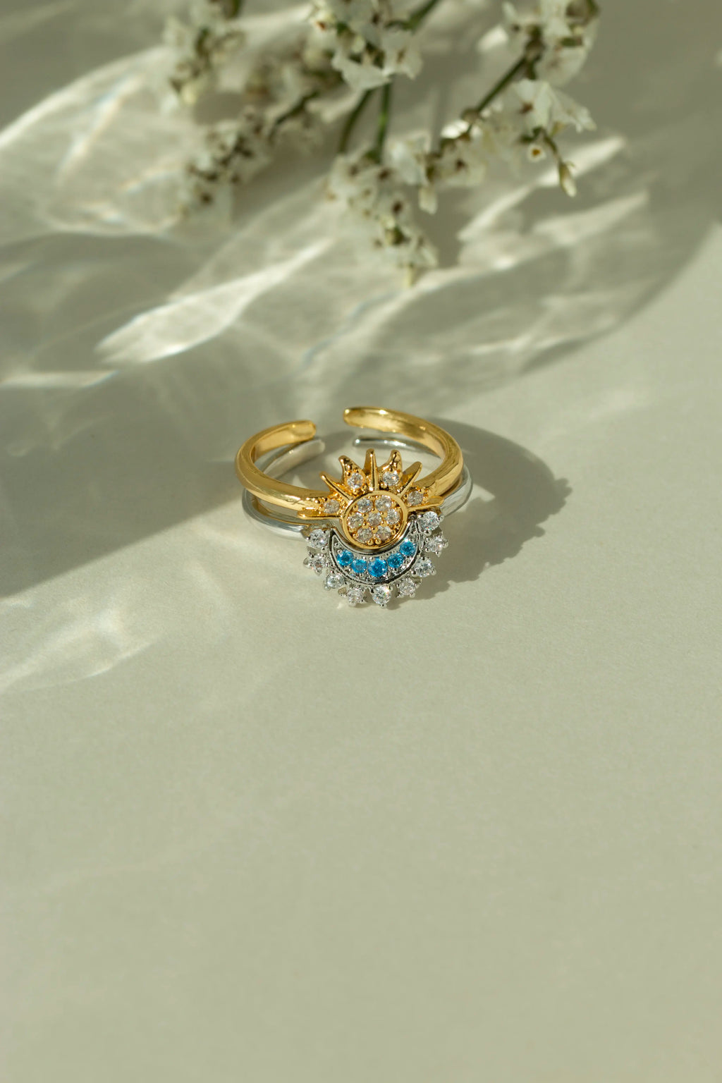 Gold sun ring and silver crescent moon ring stacked together as a celestial set. Adjustable mixed metal sun and moon ring with clear and light blue crystal details on a sunlit backdrop.