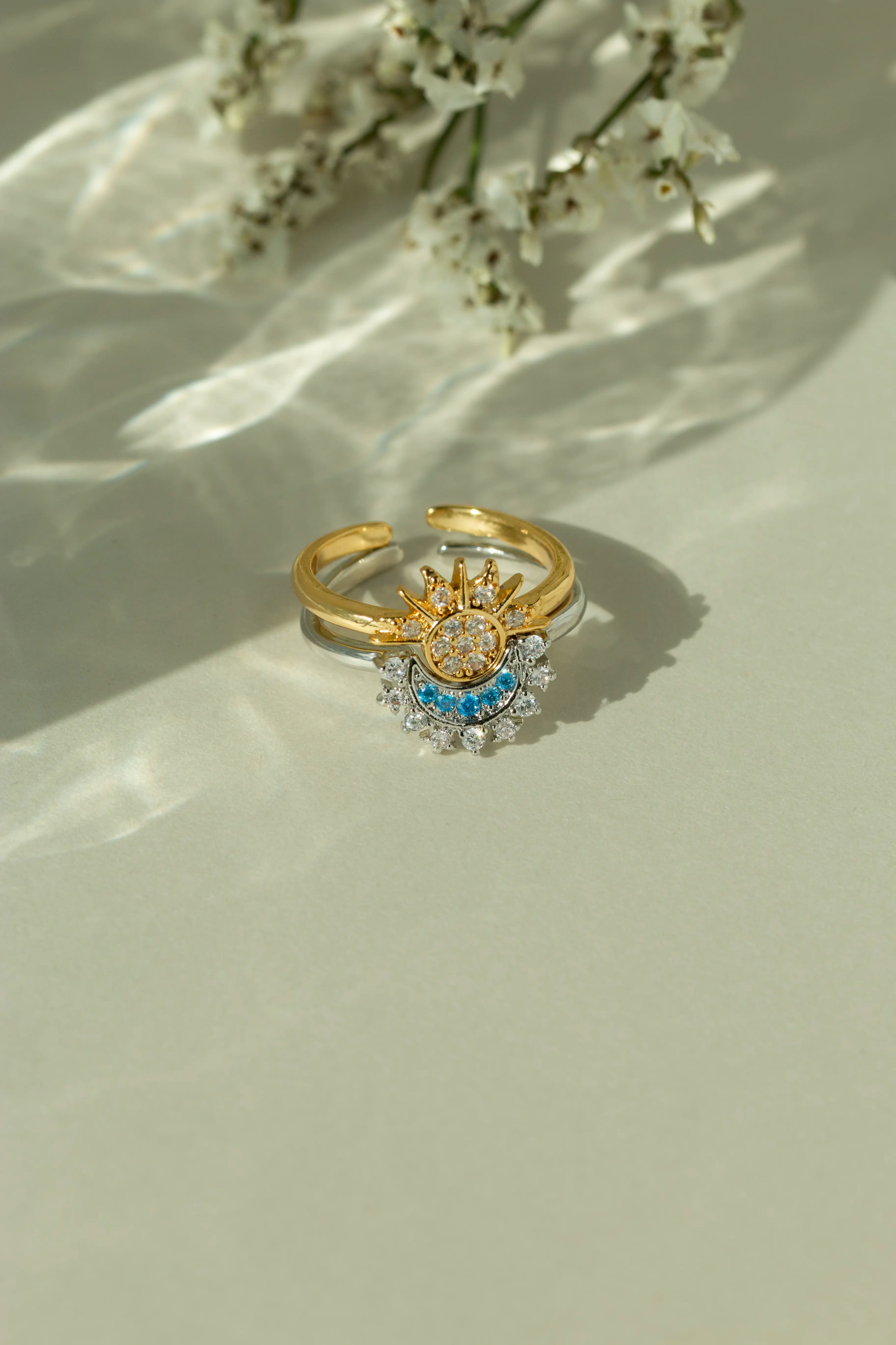 Gold sun ring and silver crescent moon ring stacked together as a celestial set. Adjustable mixed metal sun and moon ring with clear and light blue crystal details on a sunlit backdrop.