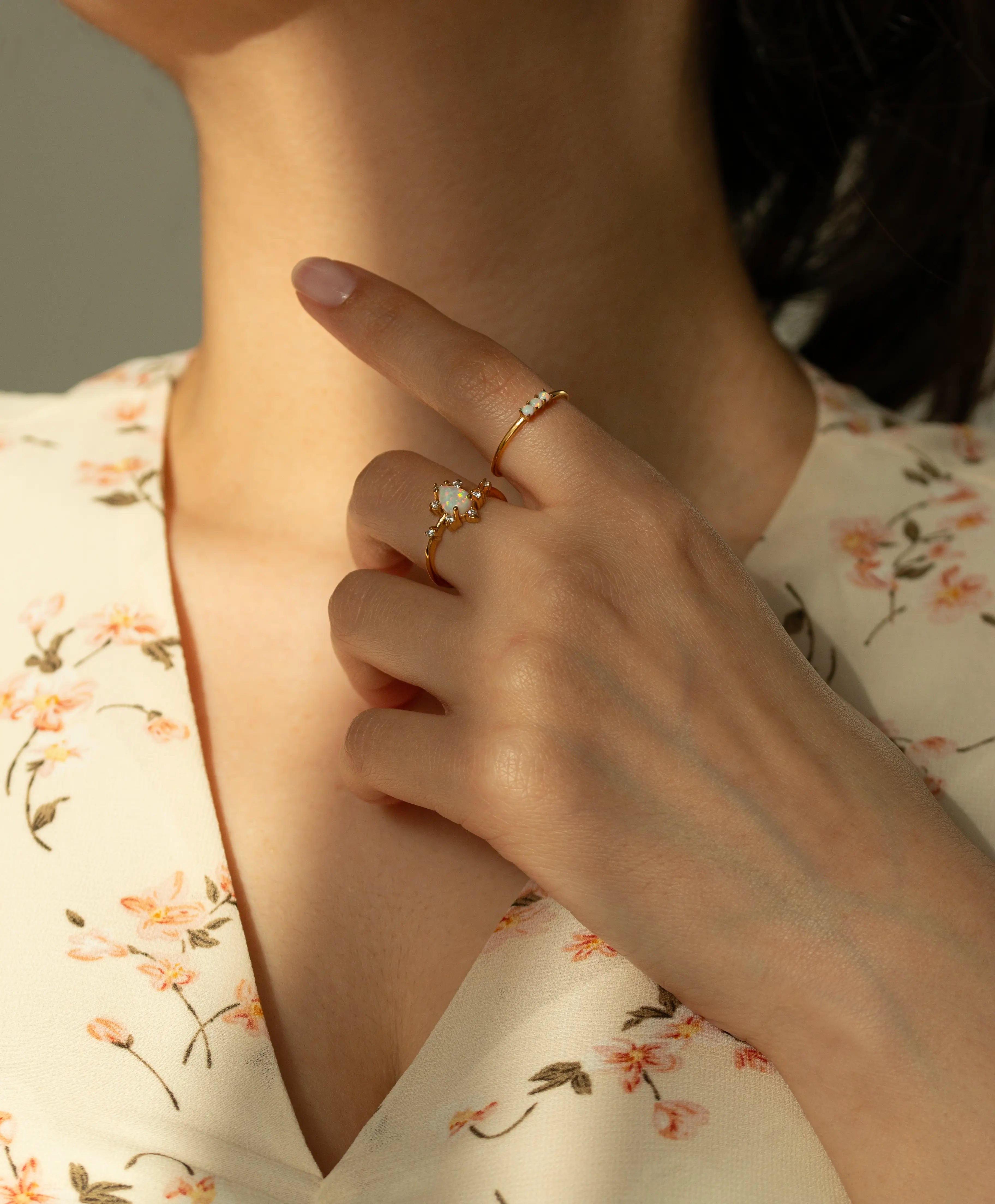 Yellow gold three stone natural opal ring. Thin minimalist gemstone stacking band styled with blurred white flowers in the background.