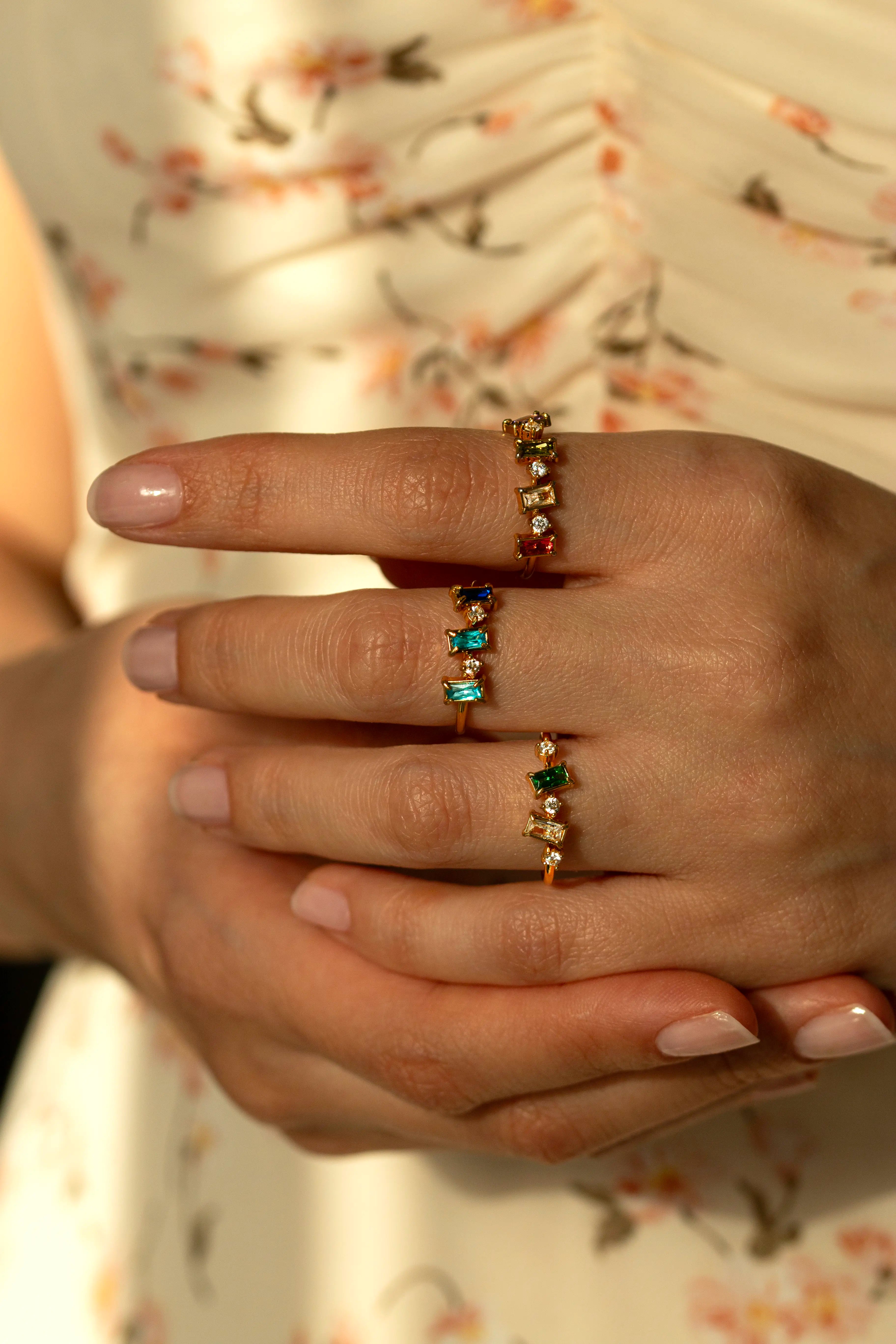 Trendy gold multi stone rings with rectangular baguette cut gems and tiny diamond accents. Aesthetic multi color birthstone jewelry cluster rings styled with white flowers under morning shadows.