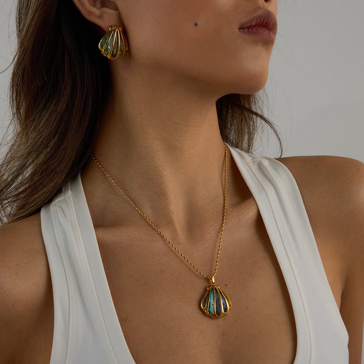 Woman wearing a gold necklace with a pendant and matching earrings against a neutral background