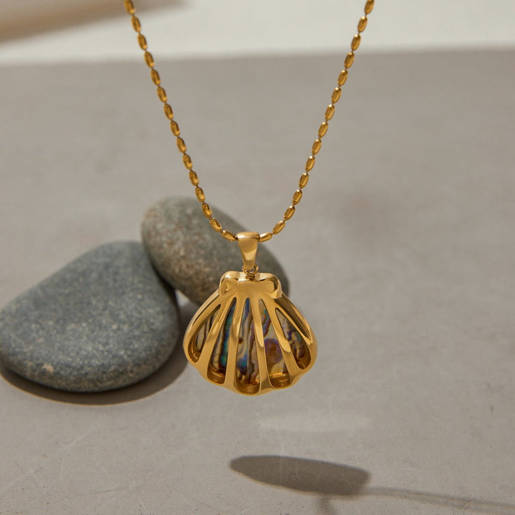 Gold necklace with a shell pendant on a neutral background