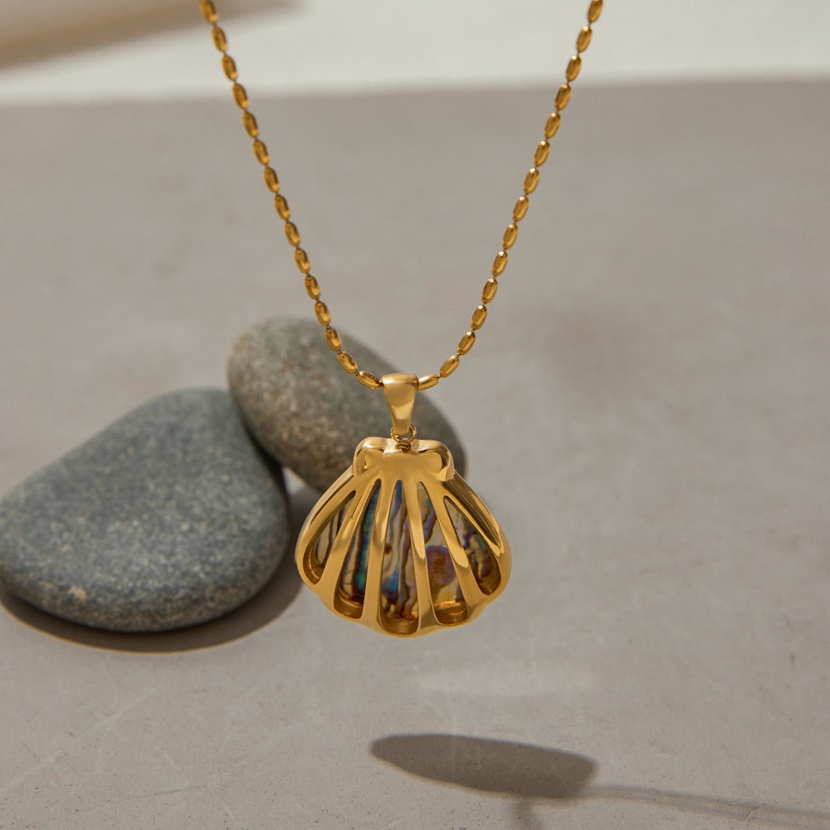 Gold necklace with a shell pendant on a neutral background