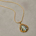 Gold necklace with a shell-shaped pendant on a beige background