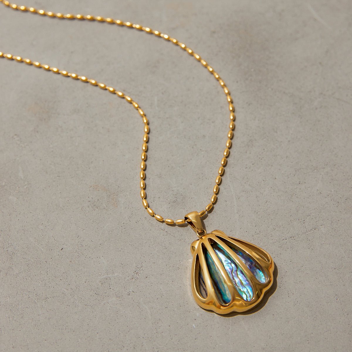 Gold necklace with a shell-shaped pendant on a beige background