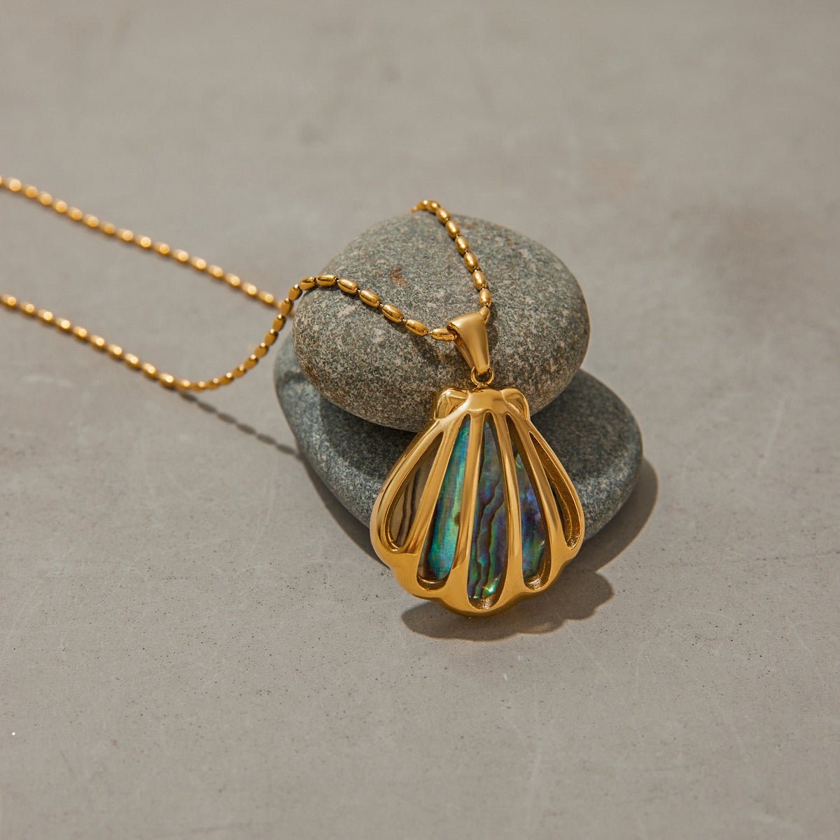 Gold necklace with a shell pendant on a stone surface