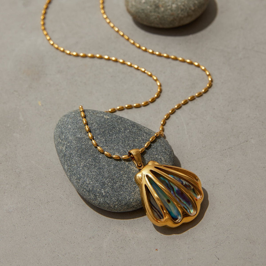 Gold necklace with a shell pendant on a gray stone surface