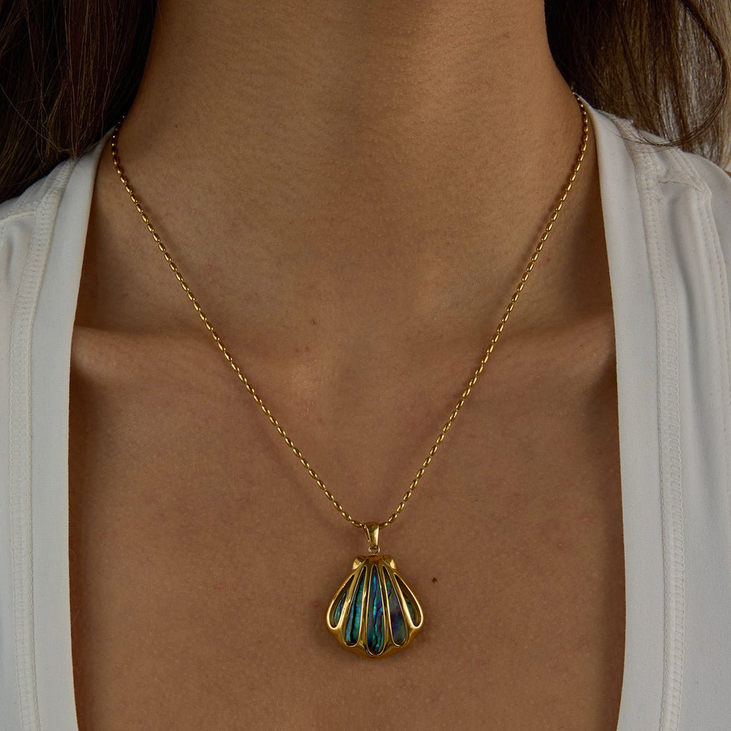 Gold necklace with a shell pendant worn by a person