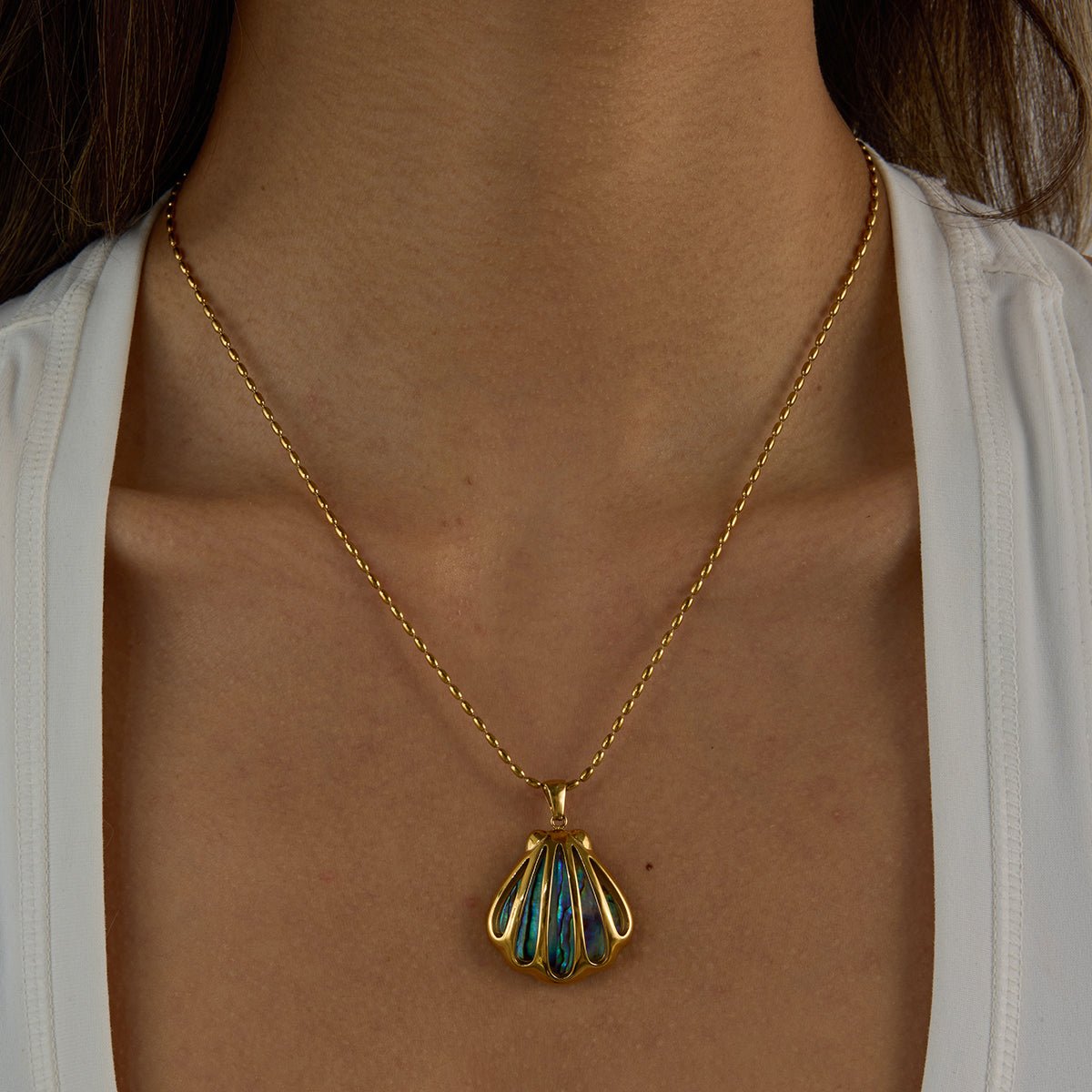 Gold necklace with a shell pendant worn by a person