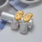 Gold and silver earrings on a white surface with a magazine in the background