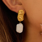 Gold earring with a white pearl drop worn by a person