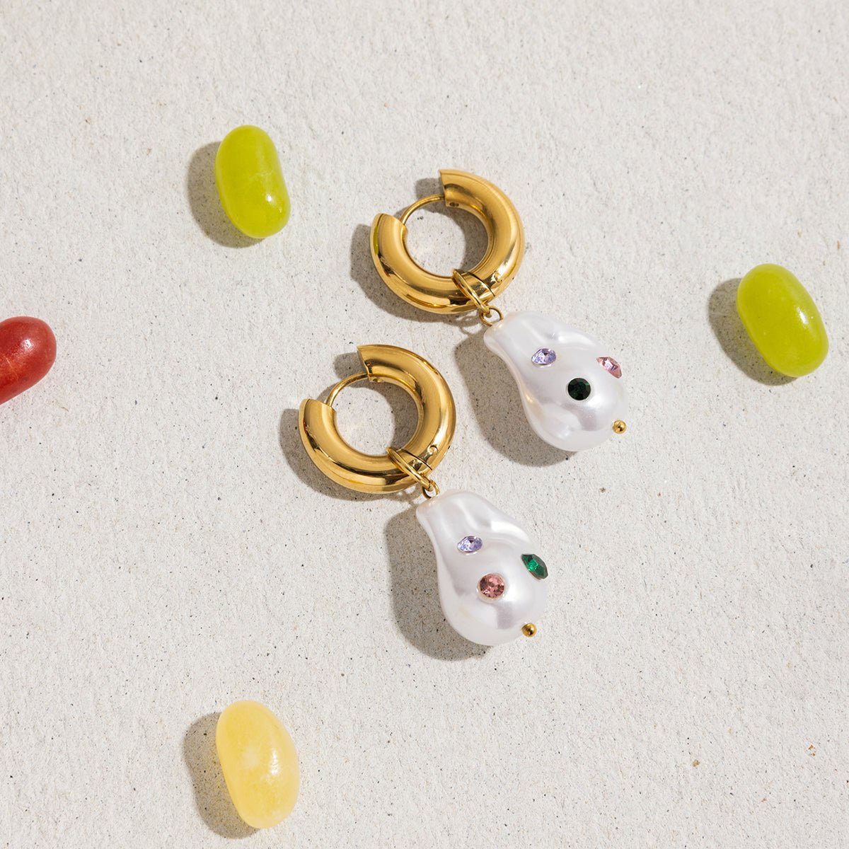 Gold hoop earrings with white teardrop-shaped charms on a textured beige surface.
