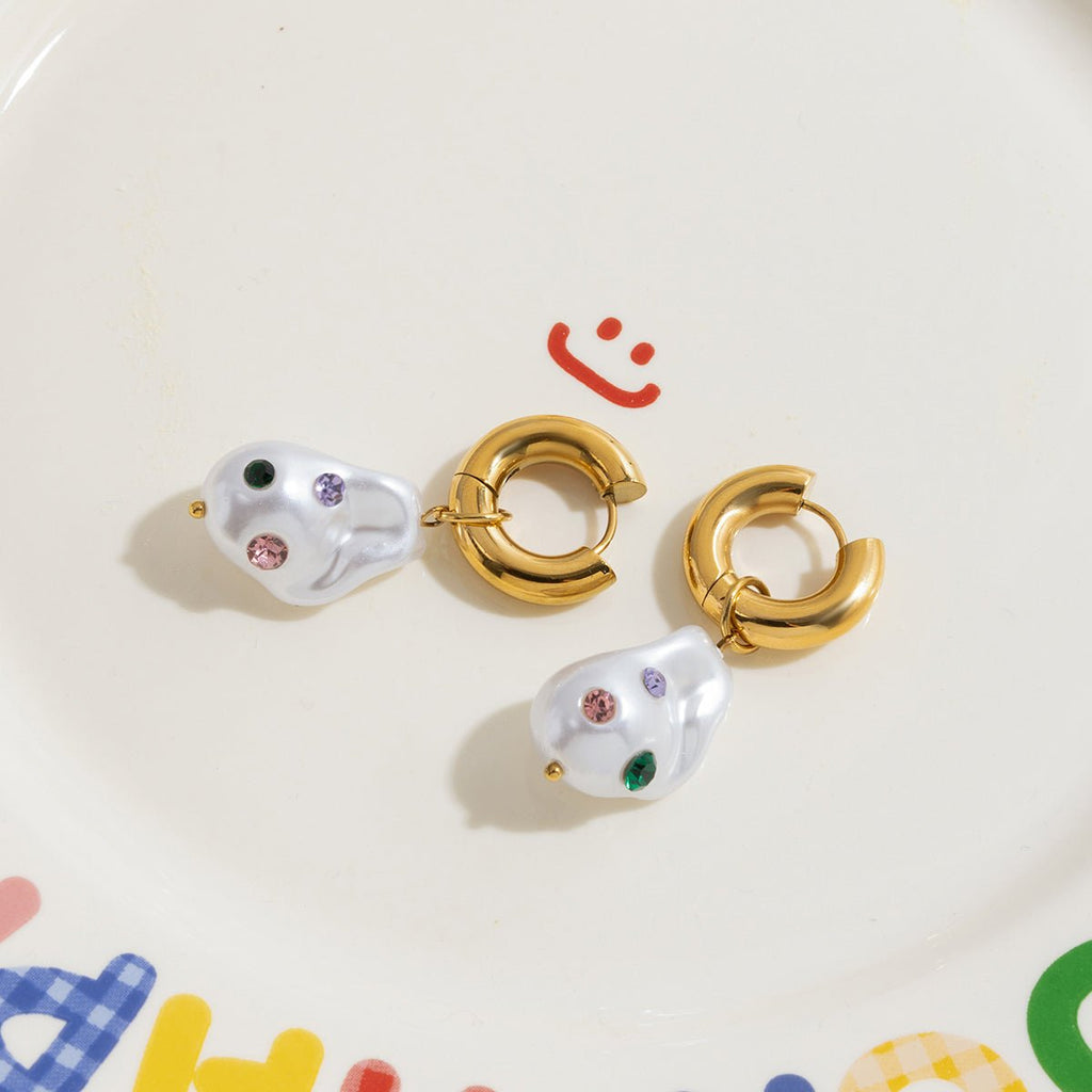 Pair of gold hoop earrings with pearl-like ends on a colorful background