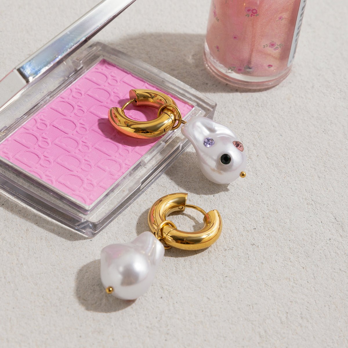 Gold hoop earrings with pearls on a pink compact mirror and white surface