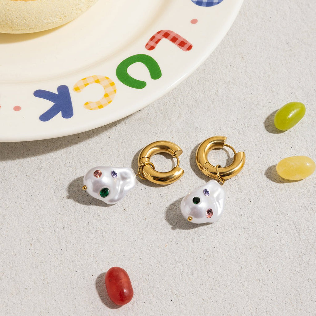 Pair of pearl earrings with gold and white accents on a light surface with colorful letters in the background.