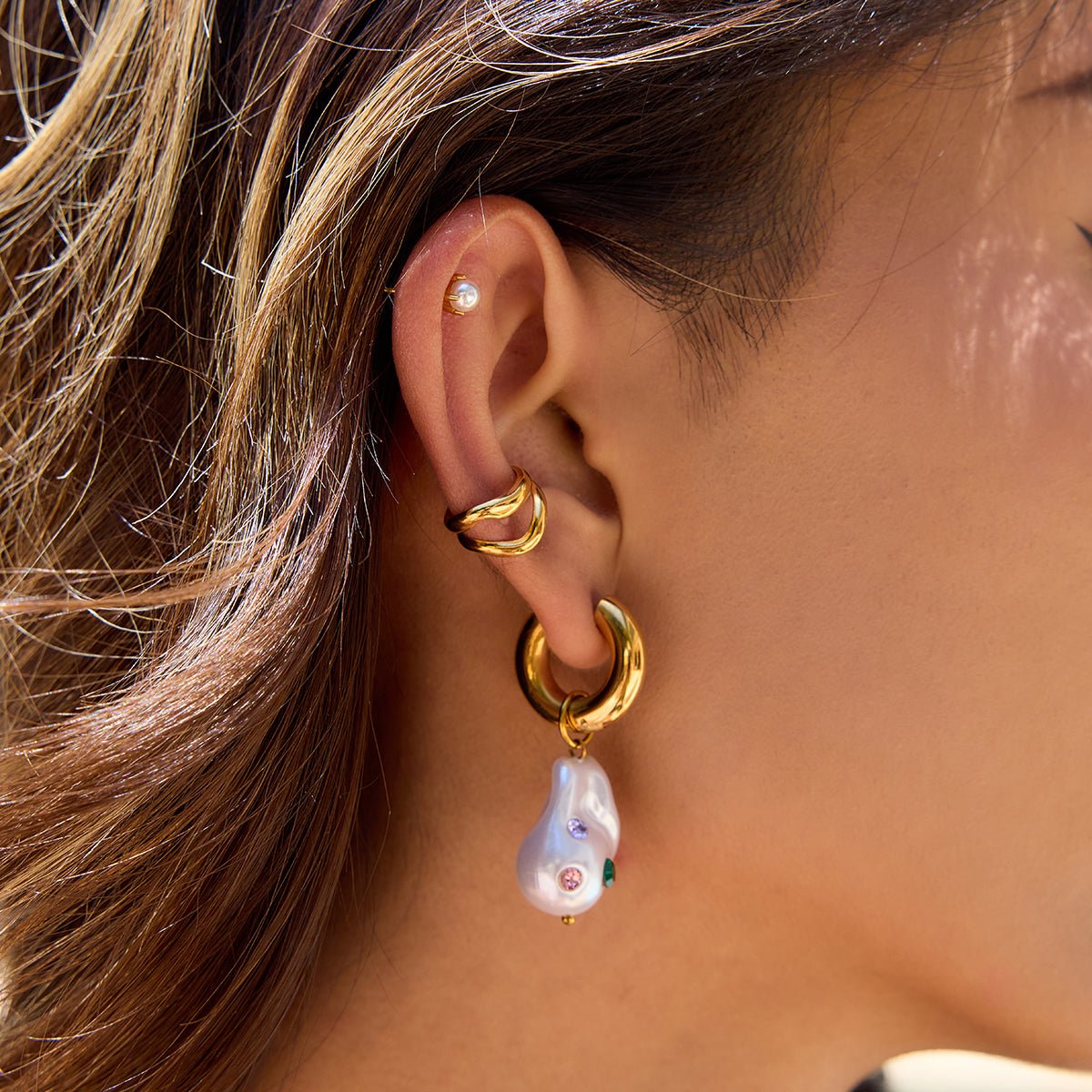 Close-up of an ear wearing gold hoop earrings with pearl drops.