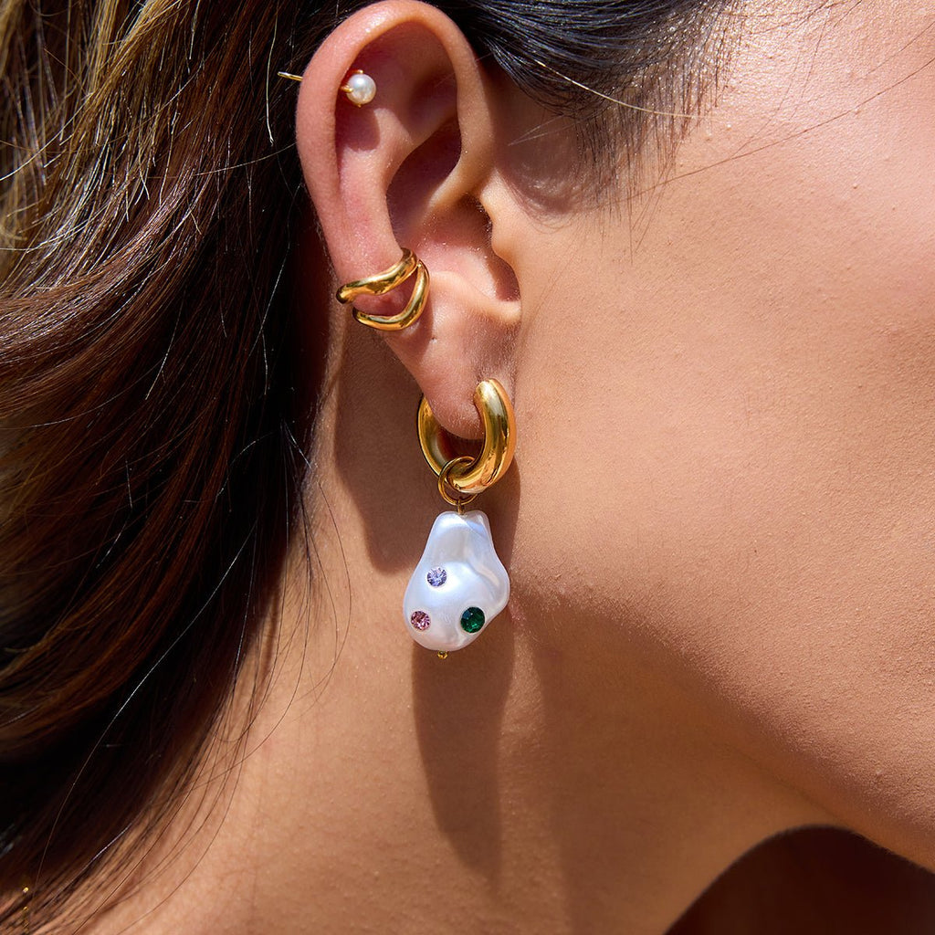 Close-up of an ear wearing gold hoop earrings with a pearl drop earring.