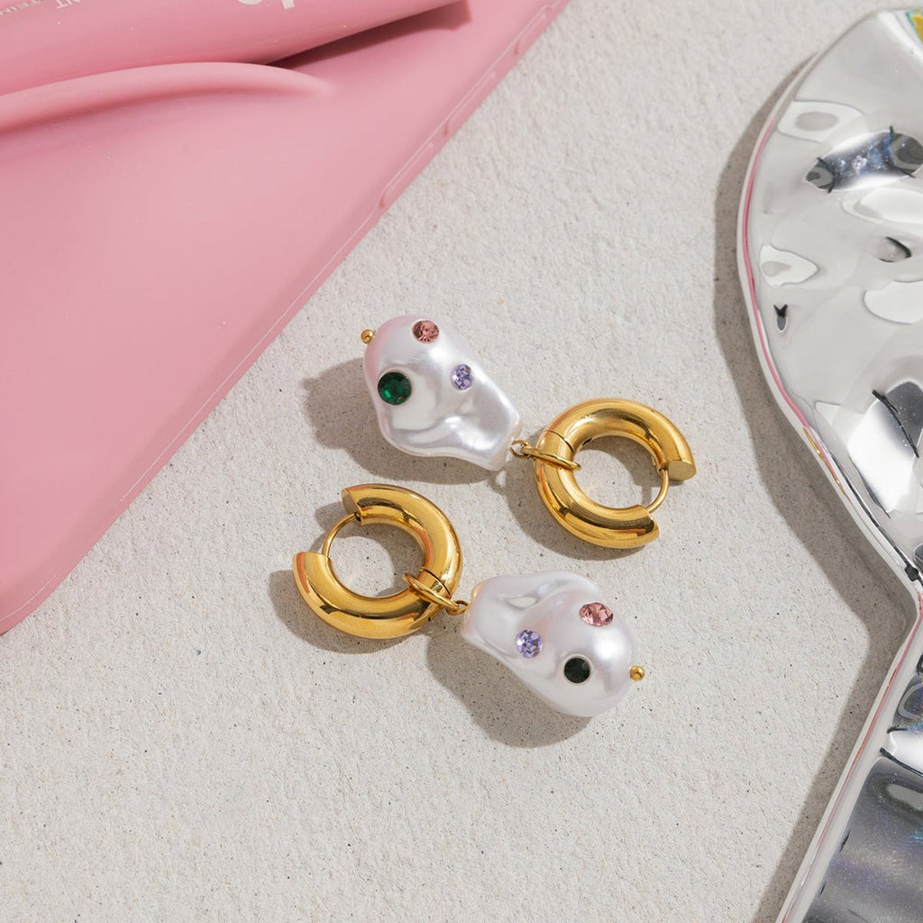 Pair of gold and pearl earrings on a textured surface with a pink background