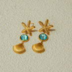 Gold starfish and shell earrings with blue gemstones on a beige background