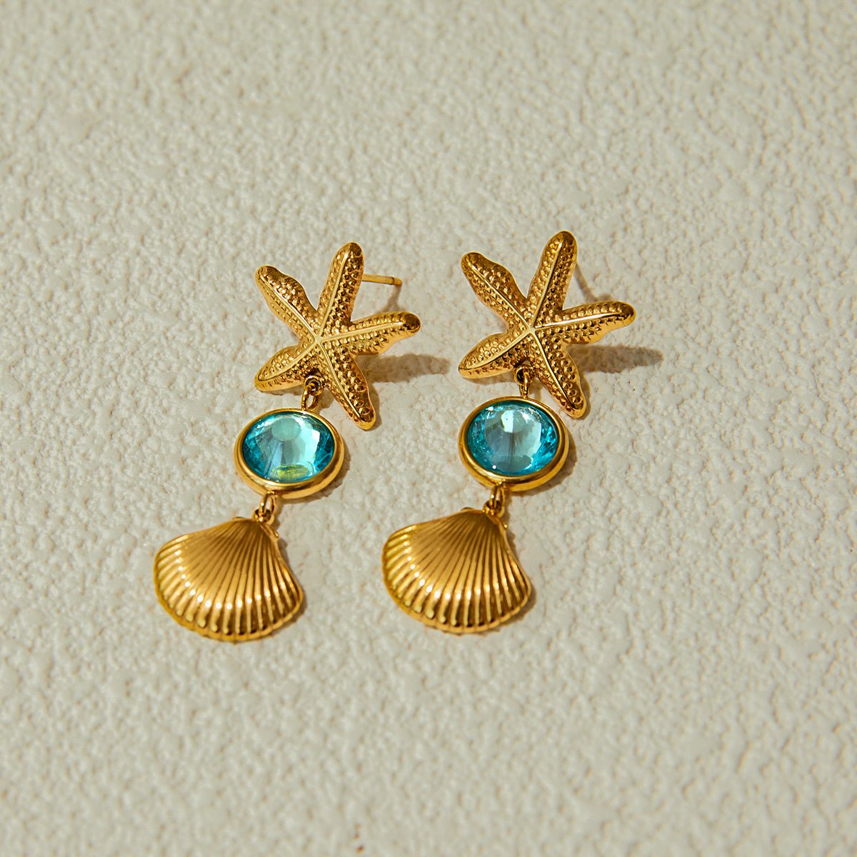Gold starfish and shell earrings with blue gemstones on a beige background