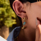 Close-up of a person wearing a gold starfish earring with a blue gemstone.