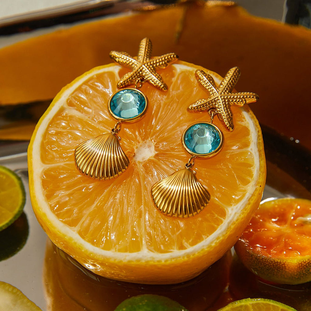 Gold earrings with starfish and shell designs on a sliced orange