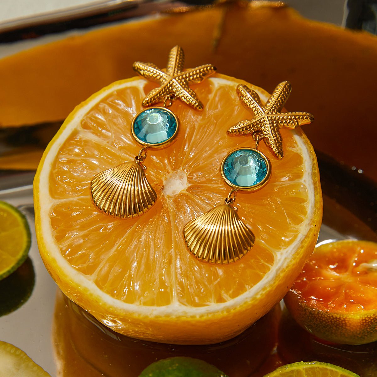Gold earrings with starfish and shell designs on a sliced orange