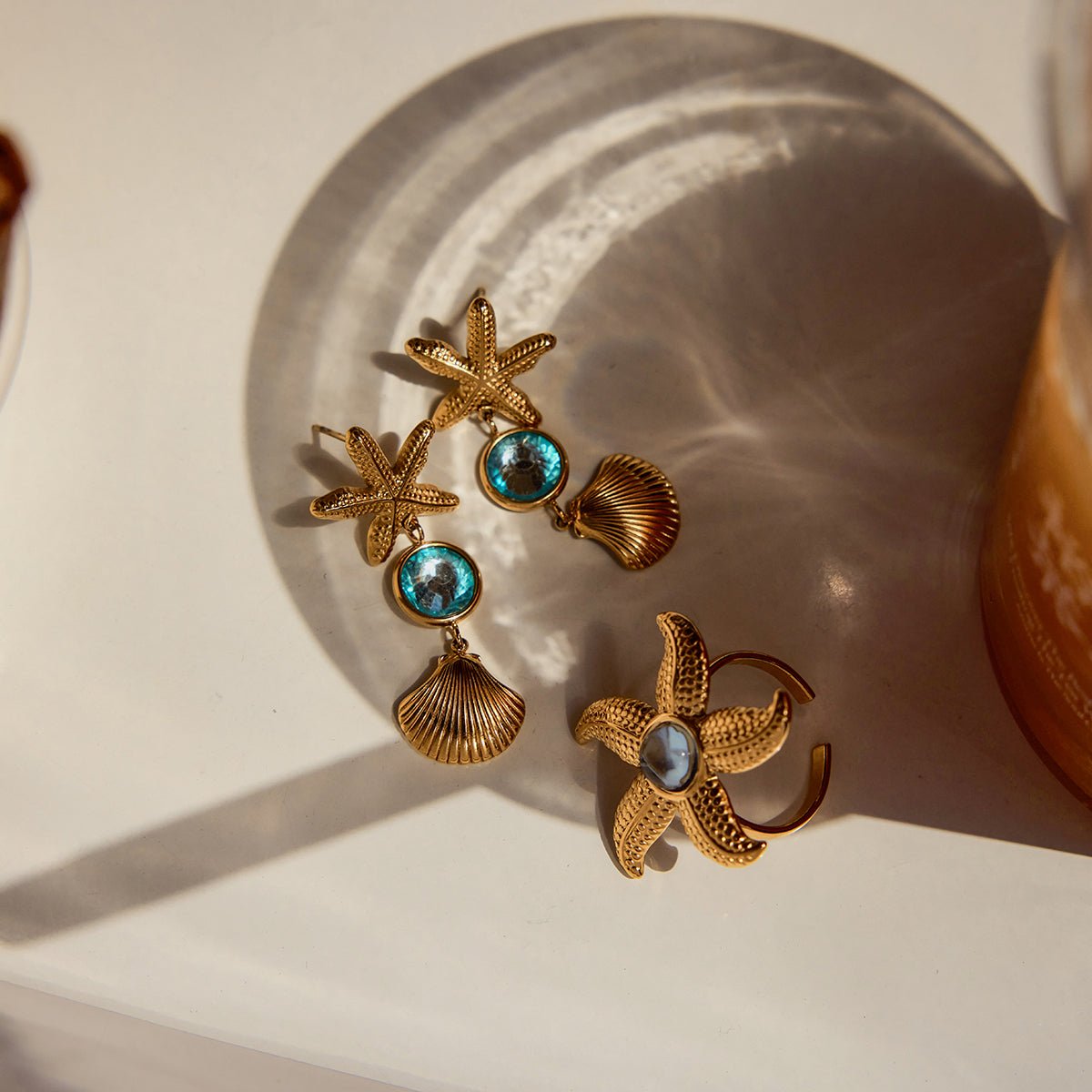 Gold earrings with starfish and shell designs on a textured surface