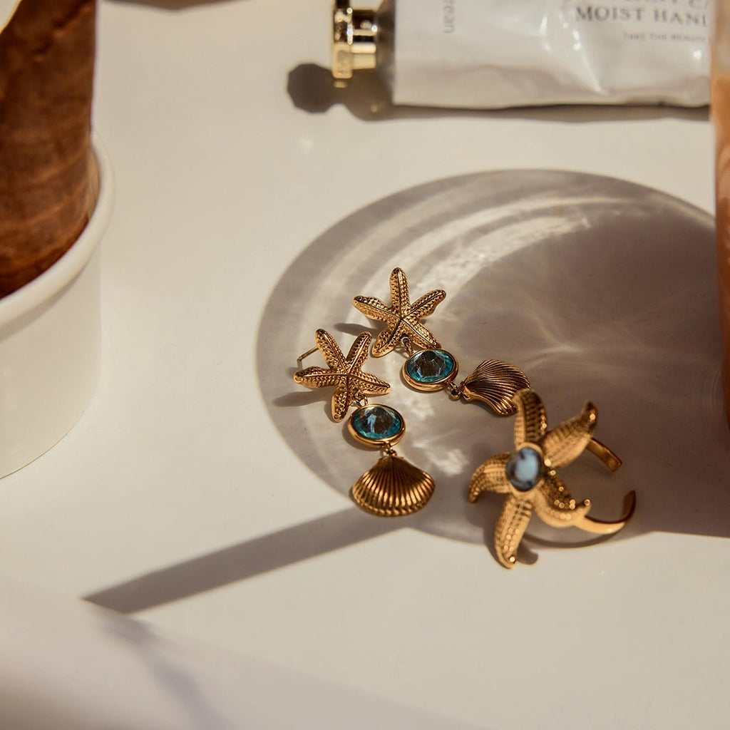Gold earrings with starfish and shell designs on a light surface