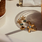Gold earrings with starfish and shell designs on a light surface