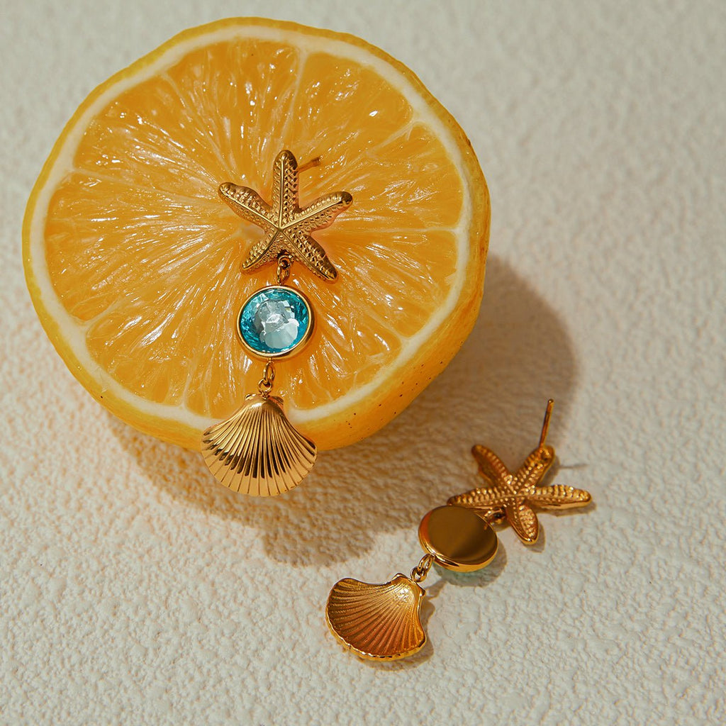 Gold earrings with starfish and shell designs on a sliced lemon.
