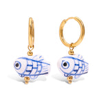 Gold hoop earrings with blue and white fish-shaped charms on a white background